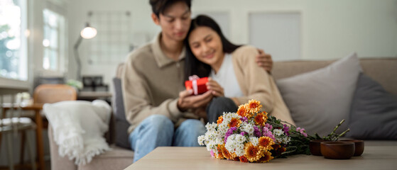 Romantic young asian couple embracing with holding flowers and smiling in living room at home. fall in love. Valentine concept