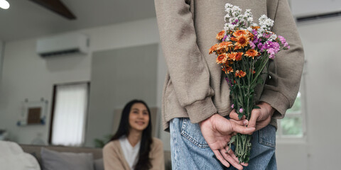Romantic young asian couple embracing with holding flowers and smiling in living room at home. fall in love. Valentine concept
