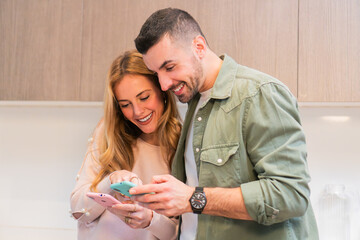 Young adult couple marriage using their smartphones at home sharing and smiling watching social...