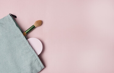 A Light Green makeup cosmetic bag with cosmetic beauty tools and product spilling out on to a pastel colored pink background Top View Copy Space