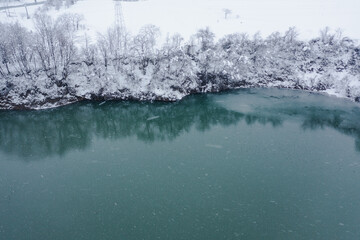 ドローン写真：雪降る冬、雪に覆われた真っ白な木々とエメラルドグリーンの川
