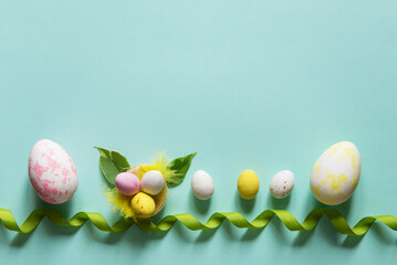 Easter concept with easter colorful eggs, nest and decorative ribbon. Delicate pastel blue empty background with copy space. Flat lay