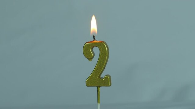 close up time lapse on gold number twobirthday candle melted on a white background.
