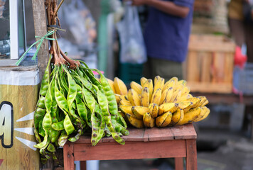 A bunch of stink bean and a stack of banana in the background being sold at the traditional market