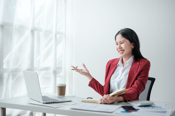 Portrait of smile beautiful business asian woman in red suit working office desk computer. Small...