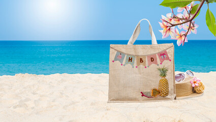 Happy Birthday bunting flag on jute bag with tropical fruit pattern on beautiful sandy beach, summer holiday gift, outdoor day light