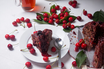 Chocolate cake with sweet cherry, cup of tea and bouquet of blue flowers on white background..