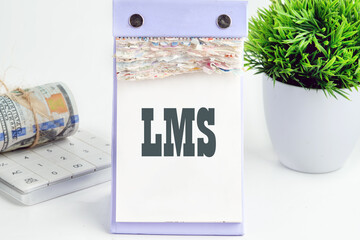 Abbreviation of Learning management system, Word LMS writing on a desktop tear-off calendar on a white background, next to a calculator with a roll of banknotes