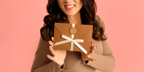 Elegant woman holding envelope Gift Certificate in hands on pink background