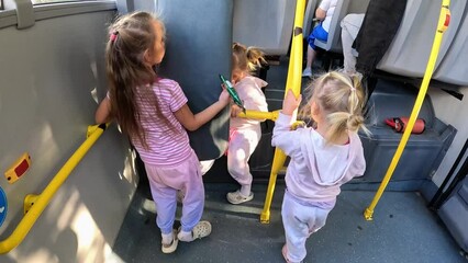 Little triplet sisters riding standing on the back of a city bus, they are dressed in sport suits - Powered by Adobe