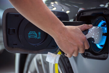 Close-up of a hand plugging in an electric vehicle charger, with glowing light indicating power...