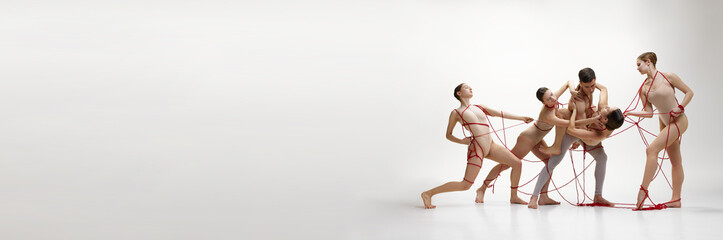 Male and female ballet dancers connected with red springs against white studio background. Support and assistance. Concept of classical dance, modern style,. Banner. Empty space to insert text, ad