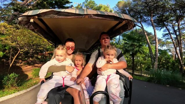 A family with three children rides a golf cart in the park, three little sisters triplets