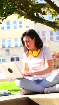 Woman studying using laptop sitting outside the campus in a sunny day