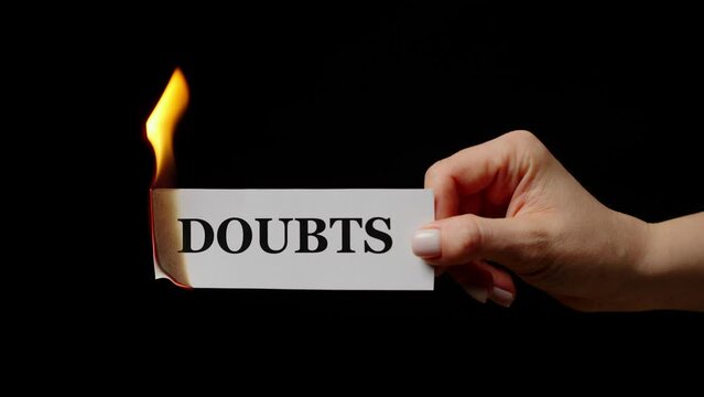 Burning white sheet with word Doubts in female hand