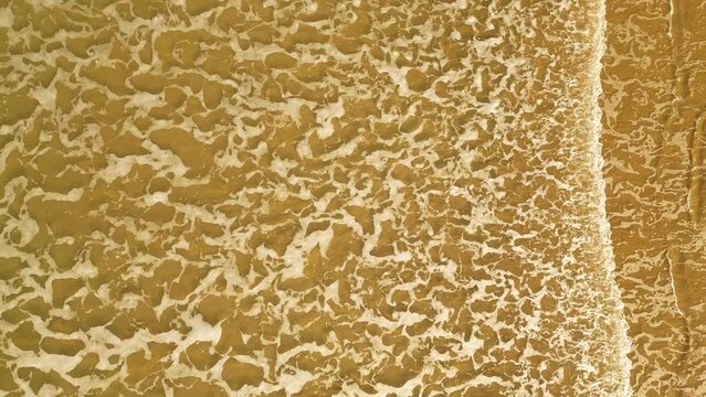 Drone shot of foamy sea waves touching the beach sand under the sunlight of the day