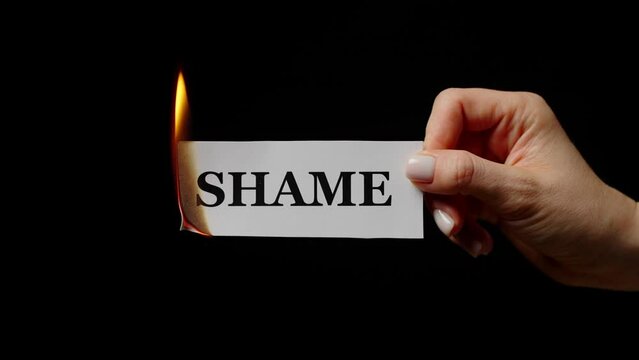 Female hand holding burning sheet with note Shame in studio