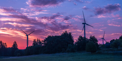 silhouettes of the rotating blades of a windmill propeller against the sunset sky. Wind energy production. Clean green energy. - obrazy, fototapety, plakaty
