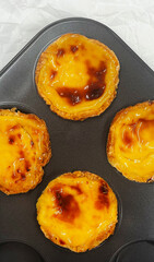 Lots of freshly baked Pastel de nata or Portuguese egg tart desserts in a baking dish. Pastel de Belme is a small pie with a crispy puff pastry crust and a custard filling. Small cupcake.