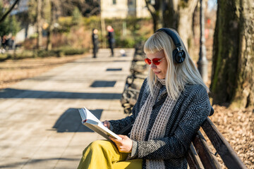 Lovely blonde young hippie girl listening music with wireless headset headphones while sitting on a...
