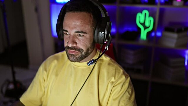 Hispanic man with beard wearing headphones in a gaming room at home during nighttime.