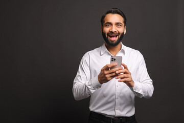 An Indian businessman in a white shirt beams with joy while using his smartphone, indicative of...