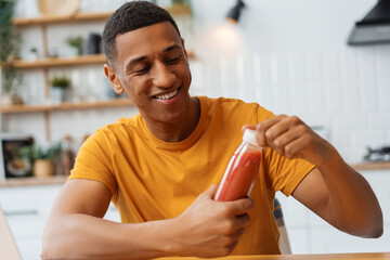 Portrait of young African American man wearing stylish yellow t shirt holding bottle of smoothie - obrazy, fototapety, plakaty