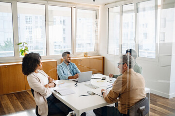 A team of four professionals are gathered around a white table in a modern office, indicative of a...