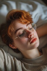 A woman with glasses relaxing on a bed. This image can be used to depict relaxation, leisure, or even reading or studying
