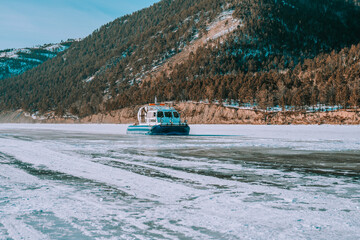 Aerohod, Khivus, a special hovercraft on the ice of the lake. View of Houseboats, on ice and snow against the background of forested mountains and blue cloudy sky. Selective focus.