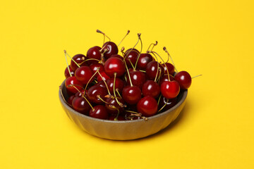 Ripe cherry fruits in a bowl on a yellow background