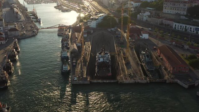 Aerial drone shot of a ship repair dry dock in Lisbon's port at sunset, situated on the north bank of the Tagus River. Shipyard is a key facility at the heart of Lisbon harbor.