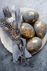 able setting. A fashionable concrete plate with a rabbit on a napkin, Easter eggs with gilding, feathers on a gray background. The concept of a Happy Easter holiday for cafes and restaurants.