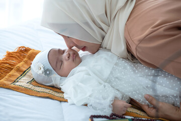 Obraz na płótnie Canvas Muslim mother kisses her newborn baby while she sleeps, both wore traditional hijabs, happy loving family concept