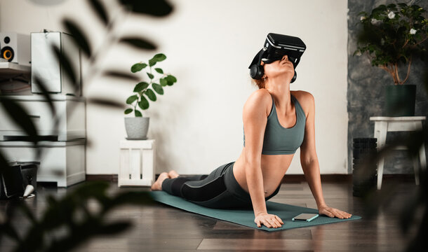 A young woman does yoga at home in a virtual reality helmet.