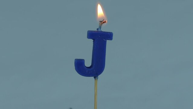 close up on a blue letter J birthday candle on a white background.
