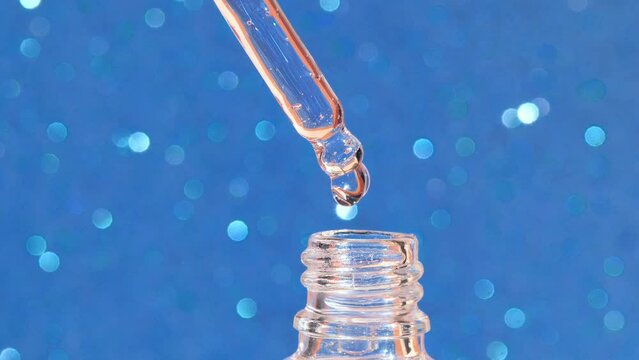 macro glass pipette with liquid fluid oil or serum drops on blue bokeh background, cosmetic liquid skin care product