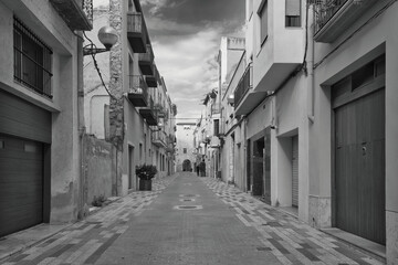 a narrow street with a person walking down it - obrazy, fototapety, plakaty