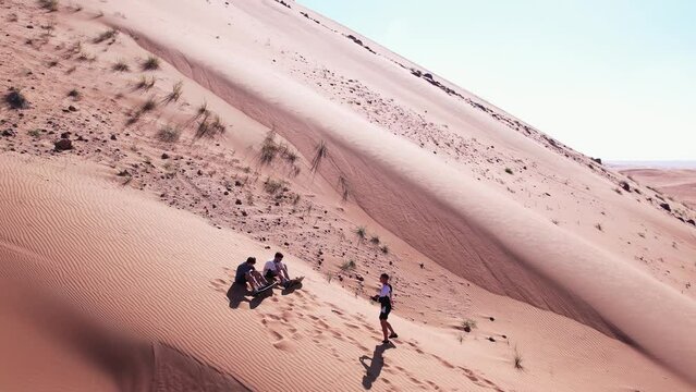 Drone view of people riding on a board on the sand dunes of the desert