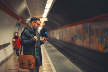 A patient adult employee using his phone while waiting for the trains
