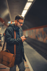 A handsome mid adult man commuting to work and waiting for the train to arrive while using his phone