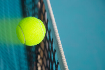 A tennis ball flies over a tennis net at high speed and leaves a trail behind it.