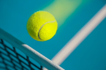 A tennis ball flies over a tennis net at high speed and leaves a trail behind it.