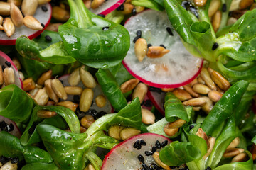 Close-up view of lamb's lettuce salad with radish, nigella seeds, and roasted sunflower seeds.
