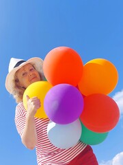 Fototapeta na wymiar A clown woman, an animator woman,in a while hat with colorful balloons against the blue sky in summer on the beach.