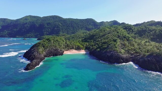 Beautiful bay with private sandy beach and clear Caribbean sea. Green mountains with reaching waves. Aerial orbit panorama.