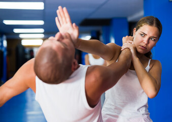 Fototapeta na wymiar Young woman practicing basic self-defense techniques while training in gym with male partner, performing palm heel strike in chin