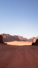 Fototapeta na wymiar Wadi Rum, Jordan, Scenic view of Arabic Middle Eastern desert against clear blue sky with sand tracks in foreground. Mountain in background. Copy space no people