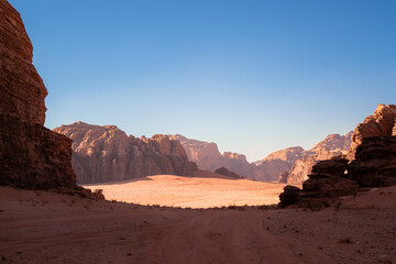 Fototapeta na wymiar Wadi Rum, Jordan, Scenic view of Arabic Middle Eastern desert against clear blue sky with sand tracks in foreground. Mountain in background. Copy space no people. Landscape horizontal