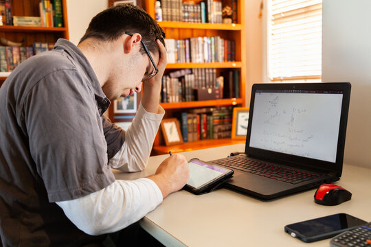 Young male uni student studying math on laptop for exams from home during covid-19